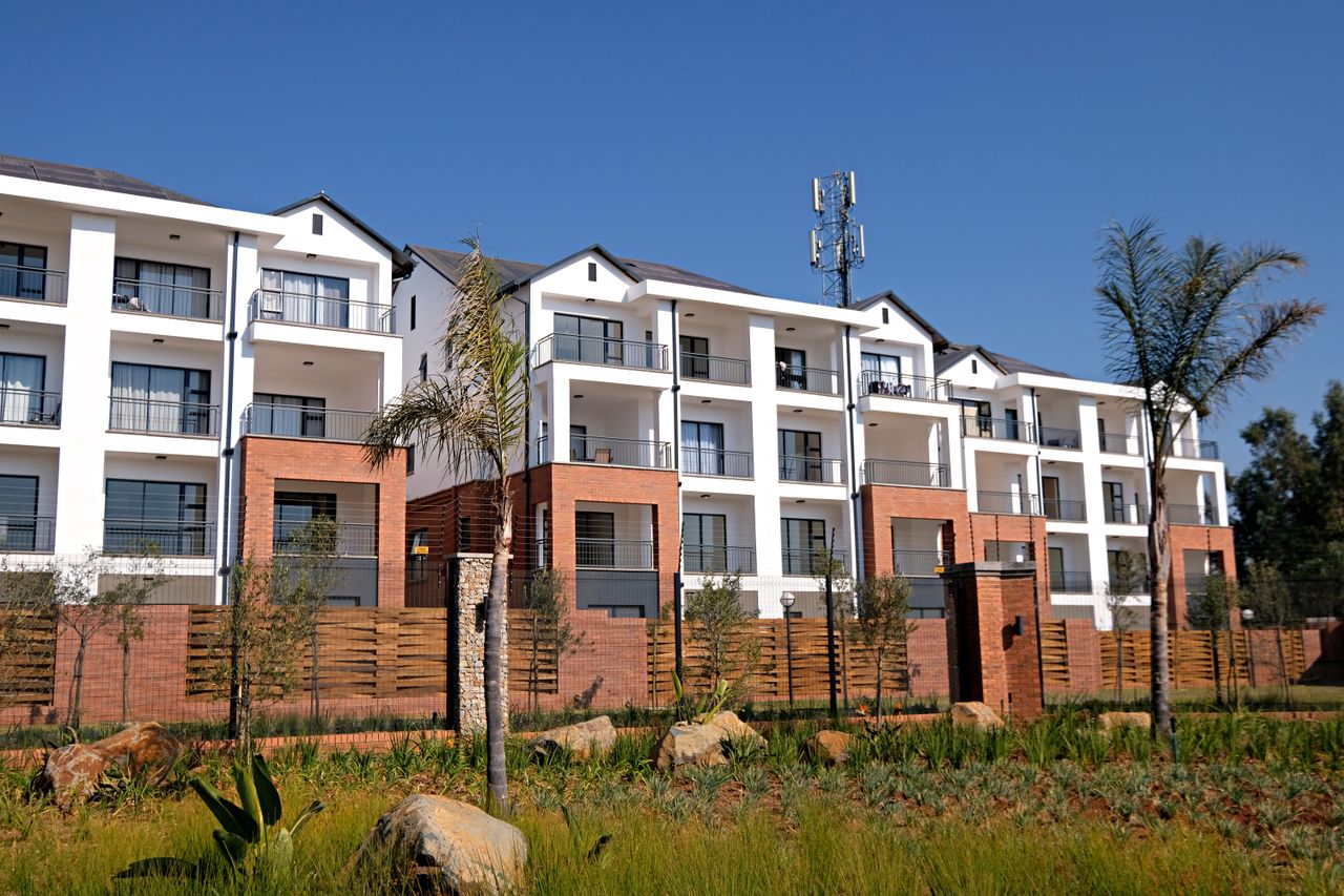 Contemporary apartment complex with garden, featuring white facade and red brick accents.