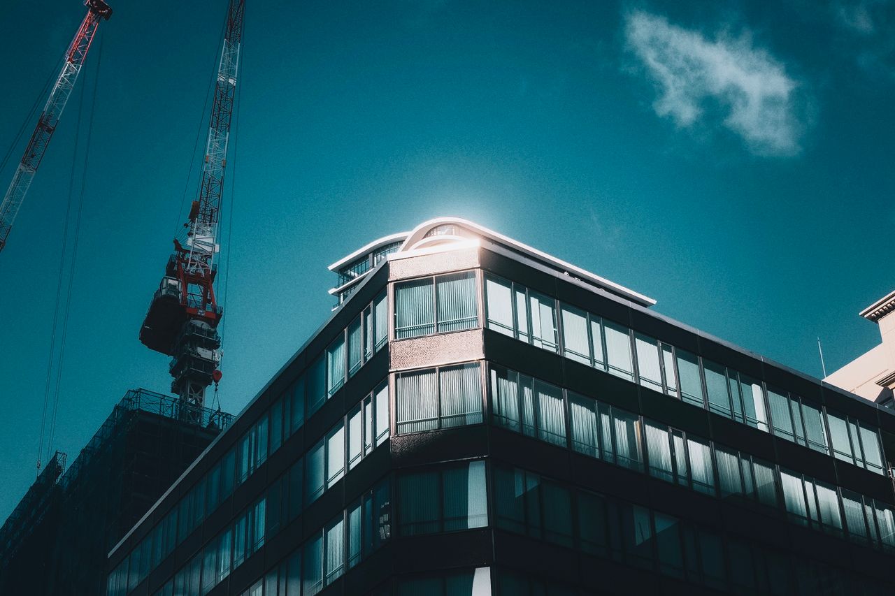 Sunlit modern building with adjacent construction crane under clear sky.