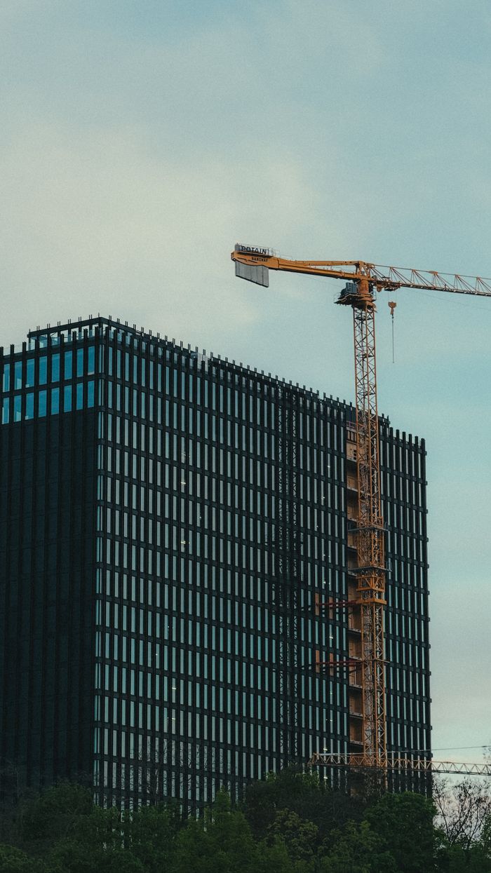 A modern skyscraper under construction with a crane against a clear sky.